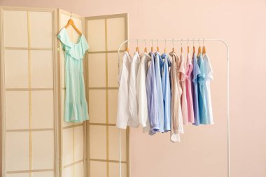 Odanın duvarında kadın giysileri olan şık katlama perdeler ve askılar.