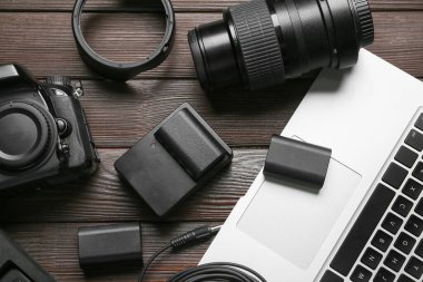 Laptop ve fotoğraf ekipmanları ahşap masada.