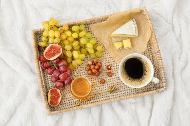 Tatlı üzümlü tepsi, atıştırmalıklar ve hafif kumaş arka planda bir fincan kahve.