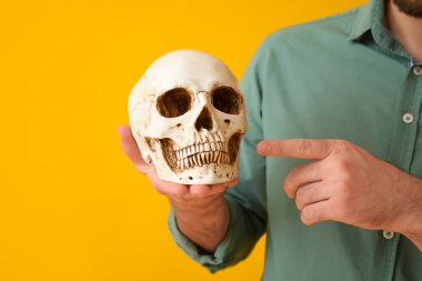 Sarı arka planda insan kafatasını gösteren yakışıklı bir adam.