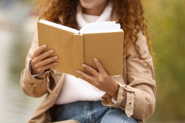 Genç Afro-Amerikalı kadın dışarıda kitap okuyor, yakın plan.