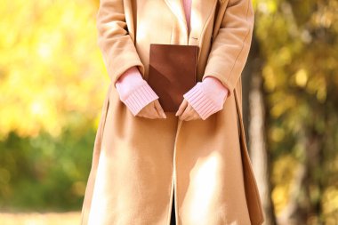 Güneşli bir günde, sonbahar parkında kitabı olan genç bir kadın, yakın plan.