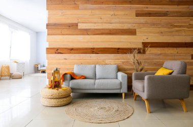 İçinde rahat kanepe, koltuk ve mum lambası olan bir oda. Pouf 'un üzerinde sonbahar yaprakları var.