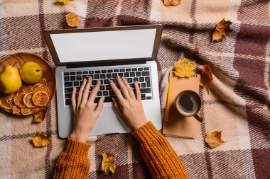 Bir fincan kahve, yemek ve yaprakları olan bir kadın kareli kumaş arka planında dizüstü bilgisayar kullanıyor.