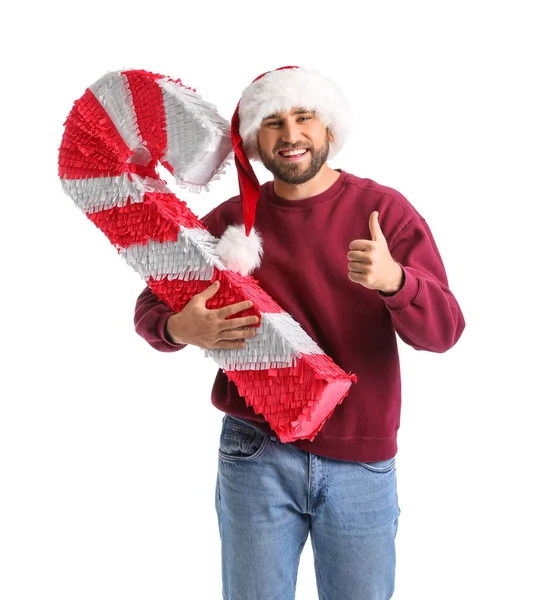 ハンサムな男でサンタの帽子とともにキャンディー杖のピナタショー親指アップ上の白い背景 — ストック写真