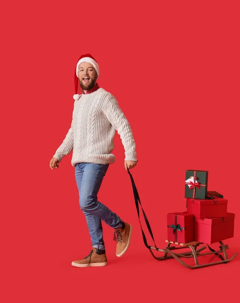 Mann Mit Haufen Weihnachtsgeschenken Auf Schlitten Vor Farbigem Hintergrund — Stockfoto