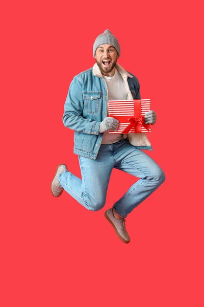 Springender Mann Mit Weihnachtsgeschenk Auf Farbigem Hintergrund — Stockfoto
