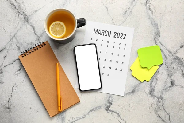 Flat lay with notebook, smartphone, cup of tea and calendar on marble background