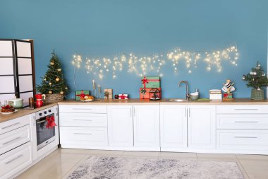Beyaz tezgahları, küçük Noel ağaçları ve parıldayan ışıkları olan şık bir mutfak.