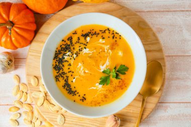 Lezzetli balkabağı kremalı çorba ve hafif ahşap arka planda tohumlar.