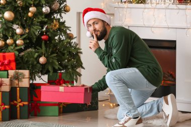 Adam oturma odasında Noel ağacının altına hediye koyuyor.