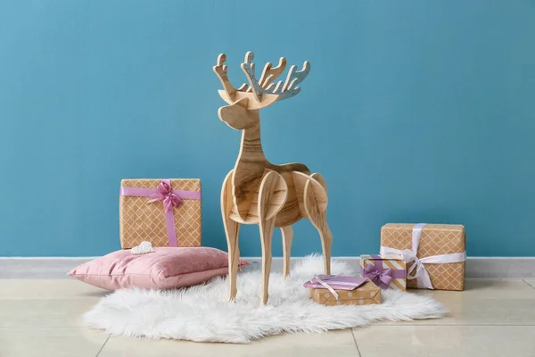 青い壁の近くにクリスマスプレゼントや枕を持つ木製のトナカイ — ストック写真