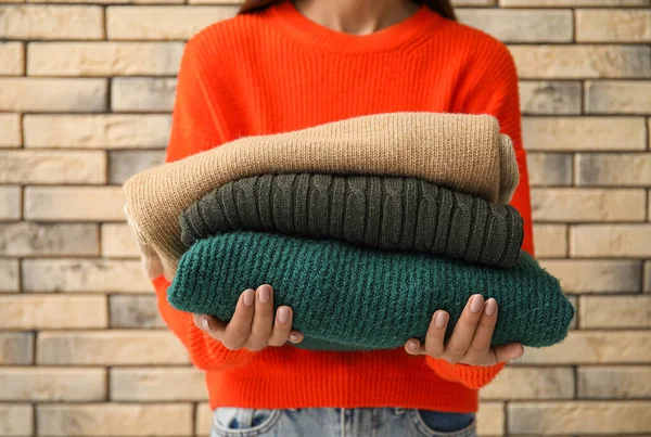 Young Woman Holding Stack Stylish Sweaters Brick Wall Background — Stock Photo, Image