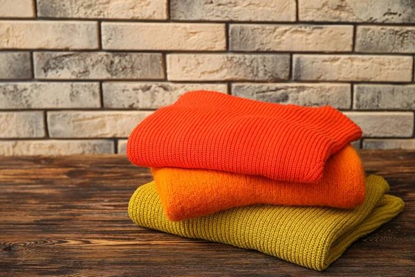 Stack Modern Sweaters Wooden Table Brick Wall Background — Stock Photo, Image