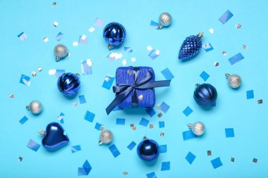 Mavi arka planda Noel hediyesi kutusu ve topları olan kompozisyon