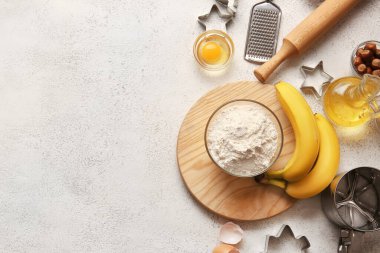 Hafif arka planda ev yapımı kurabiyeler hazırlamak için un, muz ve malzemelerle dolu bir kase.