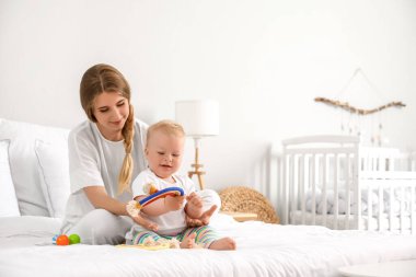 Genç anne, tatlı küçük bebeğiyle yatakta oynuyor.