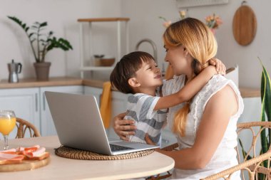 Küçük çocuk mutfakta yemek masasında annesine sarılıyor.