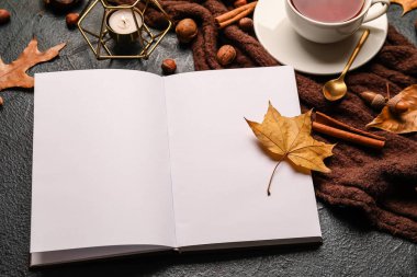 Açılmış kitap, yanan mum, bir fincan çay ve karanlık masada sonbahar dekoru.
