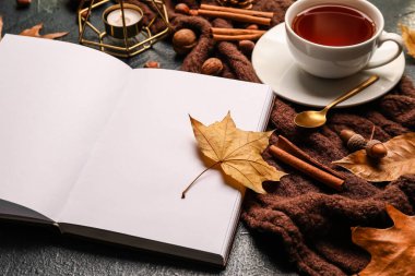 Açılmış kitap, mum, çay fincanı ve sonbahar dekoru.