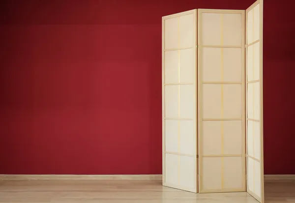 Stylish folding screen near red wall