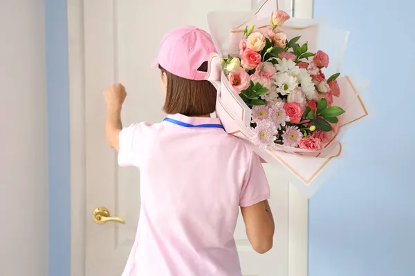 Female courier with bouquet of flowers knocking at customer\'s door
