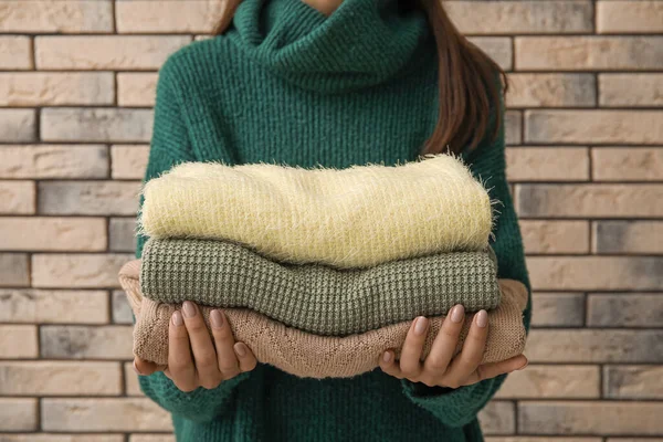若いです女性保持スタックの柔らかい現代的なセーター上のレンガの壁の背景 — ストック写真