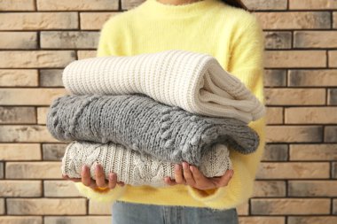 Woman holding stack of knitted sweaters on brick wall background clipart