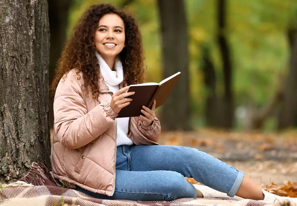 Genç Gülümseyen Afro Amerikalı Kadın Elinde Kitapla Sonbahar Parkında Oturuyor — Stok fotoğraf