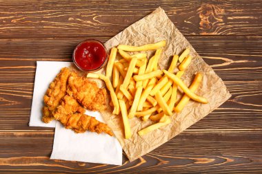 Lezzetli kızarmış tavuk kanatları, patates kızartması ve ahşap masada domates sosu.