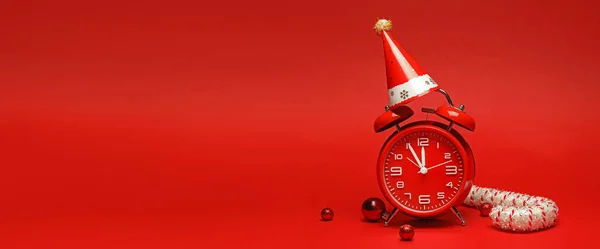 Wecker Mit Partyhut Und Weihnachtsdekoration Auf Rotem Hintergrund Mit Platz — Stockfoto