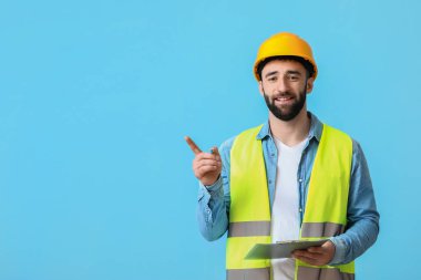 Mavi arkaplandaki bir şeyi gösteren panosu olan inşaat işçisi