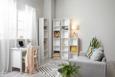 Modern iş yeri, kanepe ve büyük raf ünitesi olan aydınlık oturma odasının içinde.