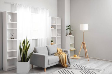 Gri kanepe, lamba ve raf üniteleriyle aydınlık oturma odasının içinde.