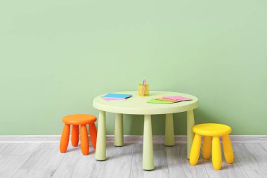 Çocuk odasındaki renkli duvarın yanında sandalye ve kırtasiye malzemeleri olan masa.
