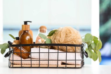 Kozmetik ürünleri şişeleri, diş fırçaları, havlu, banyo süngeri ve okaliptüs dallarıyla dolu bir sepet.