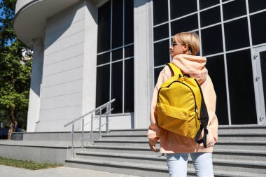 Şık kapüşonlu ve açık havada sırt çantalı bir bayan öğrenci.