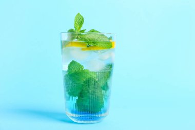 Renkli arkaplanda naneli ve limonlu bir bardak soğuk su.