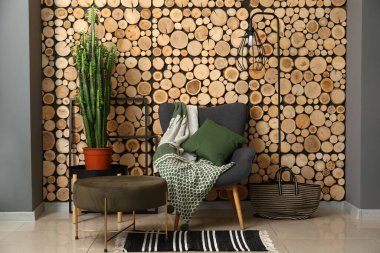 Tahta duvarın yanında yastıklı, ekoseli ve yeşil kaktüslü bir koltuk.