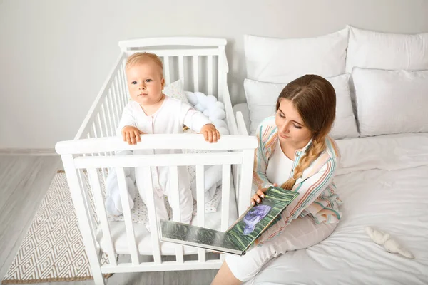 Genç anne beşikteki küçük bebeğine kitap okuyor.