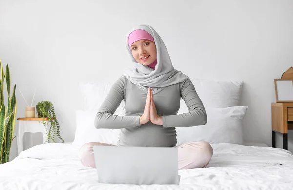 带着手提电脑在家里床上沉思的穆斯林孕妇 — 图库照片