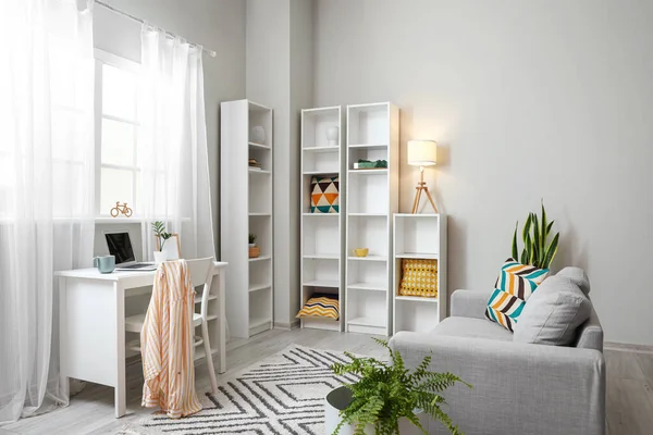 Modern iş yeri, kanepe ve büyük raf ünitesi olan aydınlık oturma odasının içinde.