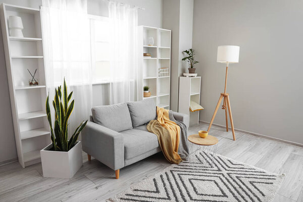 Interior of light living room with grey sofa, lamp and shelving units