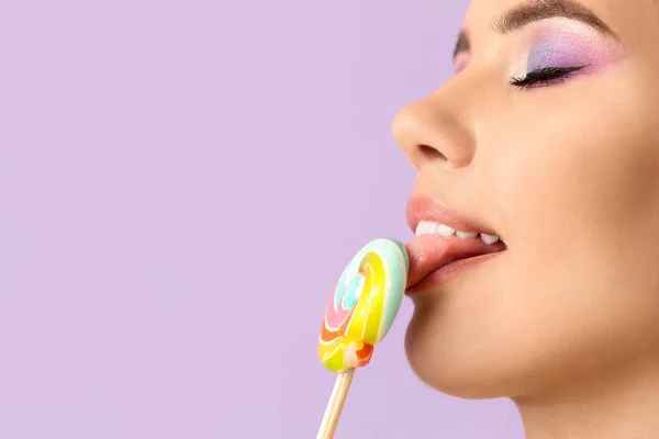 美丽的年轻女子在紫丁香背景下吃甜棒棒糖 — 图库照片