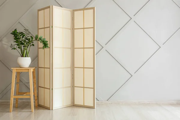 Stylish folding screen in room interior on wall background