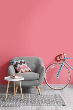 Gri koltuk, bisiklet ve pembe duvarın yanında kitapları olan masa