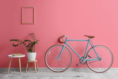 Modern bisiklet, ev bitkisi ve pembe duvarın yanındaki masa