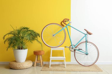 Modern bisiklet, merdiven, tabure ve çiçek rengi duvarın yanında.