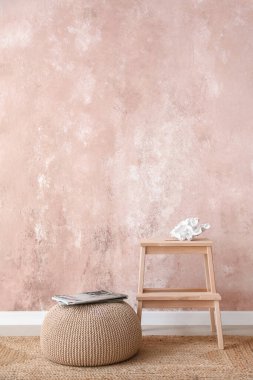 Ahşap merdiven taburesi ve pembe duvarın yanındaki şarjörlü puf.