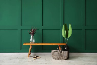 Vazolarla ahşap bank, parmak arası terlikler ve yeşil duvarın yanında çanta.